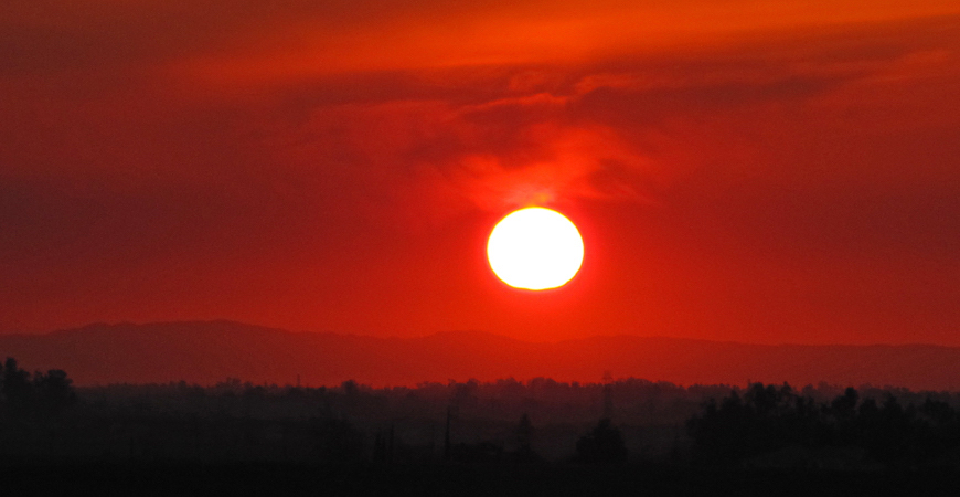 Sun setting in red-orange sky over darkened mountain range as seen from UC Merced's Kolligian Library.