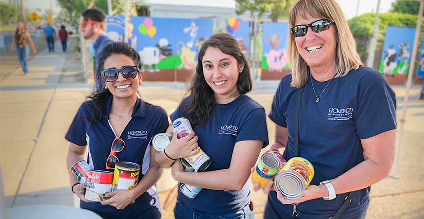 Three women from UC Merced hold canned foods that were donated during a food drive during the Merced County Fair.
