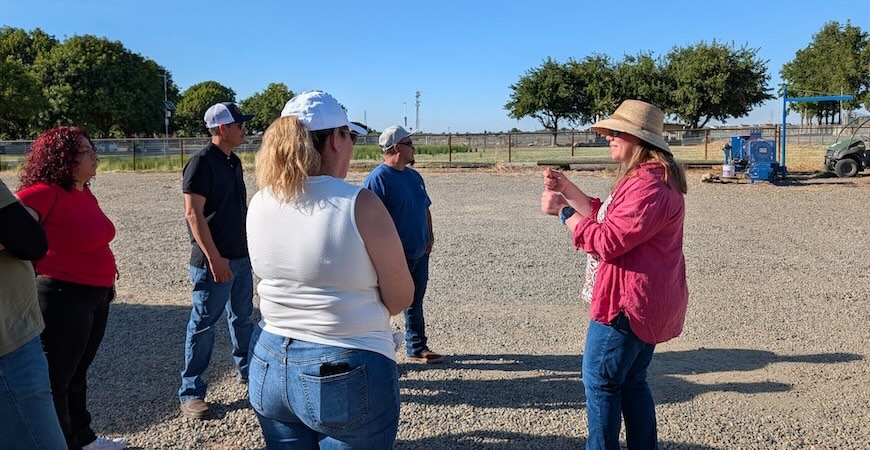 UC Merced postdoctoral researcher Kimberly Gibson is pictured in a red shirt and straw hat talking to a crowd of people
