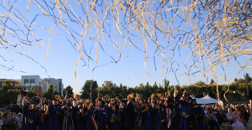Blue and gold streamers fly over the heads of graduates at UC Merced's Graduate Division commencement ceremony.