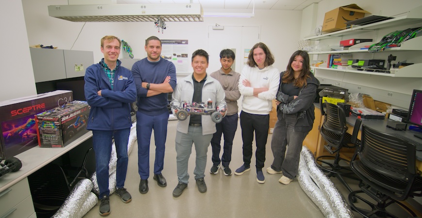 Professor Ross Greer is pictured with five students and an autonomous model car in his lab at UC Merced.