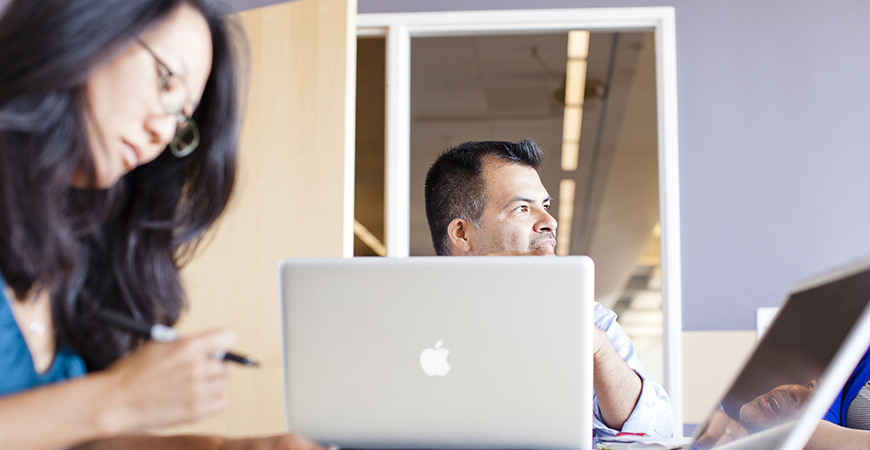 A man and a woman seated at table, using their computers.