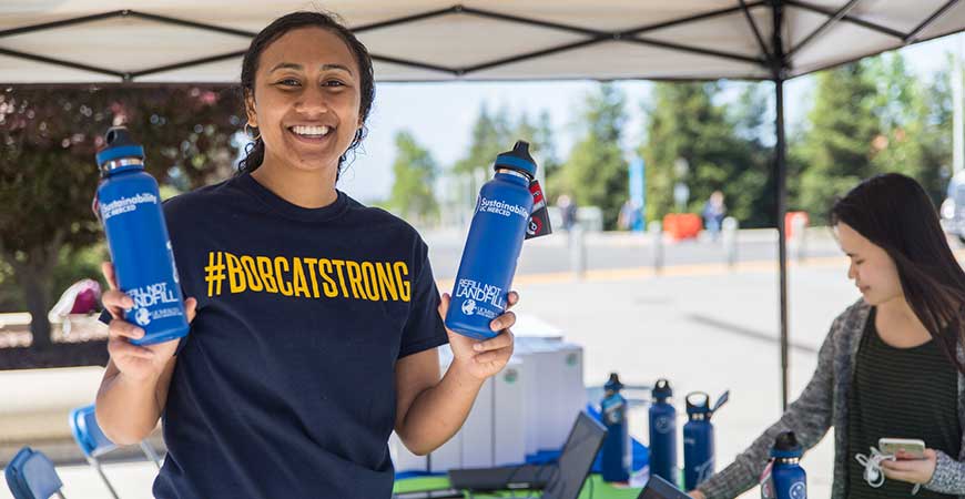 UC Staff member Breeana Sylvas poses outdoors with two reusable water bottles. 