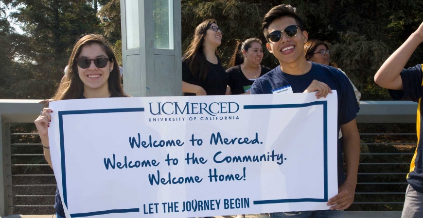Two students hold a sign that reads: Welcome to UC Merced. Welcome to the Community. Welcome Home!
