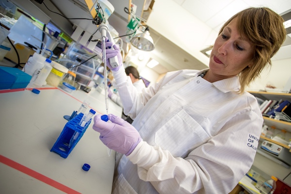 A woman in a white lab coat holding a pipet at a bench in the laboratory. 