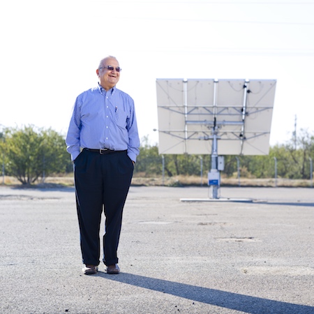A man in a blue shirt and black pants stands in front of a solar panel.