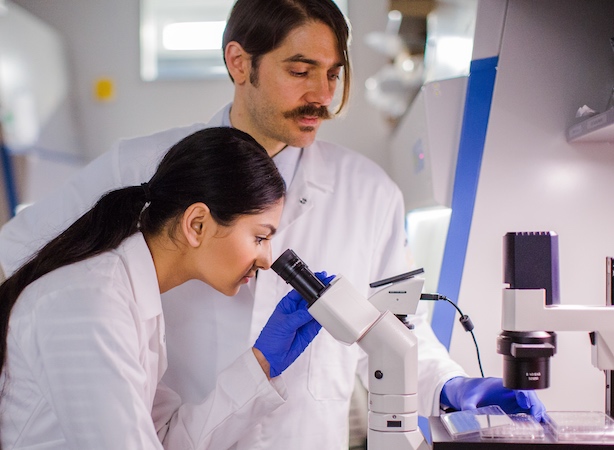 Profile view of female student looking through microscope and man looking at microscope stage next to her.