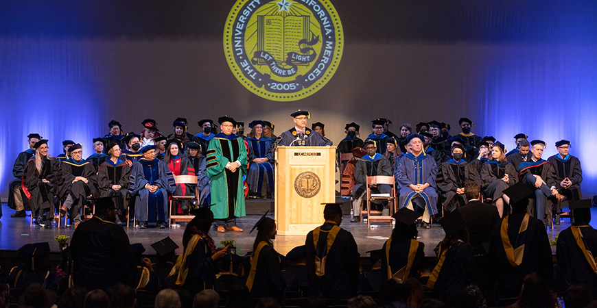 UC Merced Chancellor Juan Sánchez Muñoz stands at the podium during a commencement ceremony.