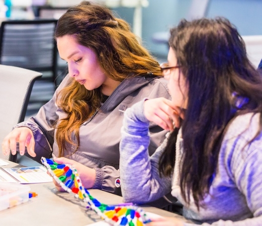 Two women at a desk building a model of DNA.