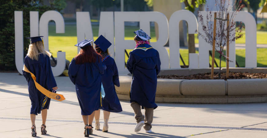 Graduating students walk pass UC Merced sign
