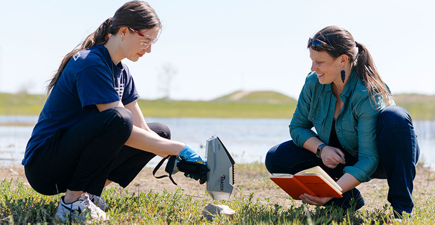 Professor Claire Lukens, right, and recent graduate Kolleen Peyakov measure the geochemistry of a rock using an XRF spectrometer.