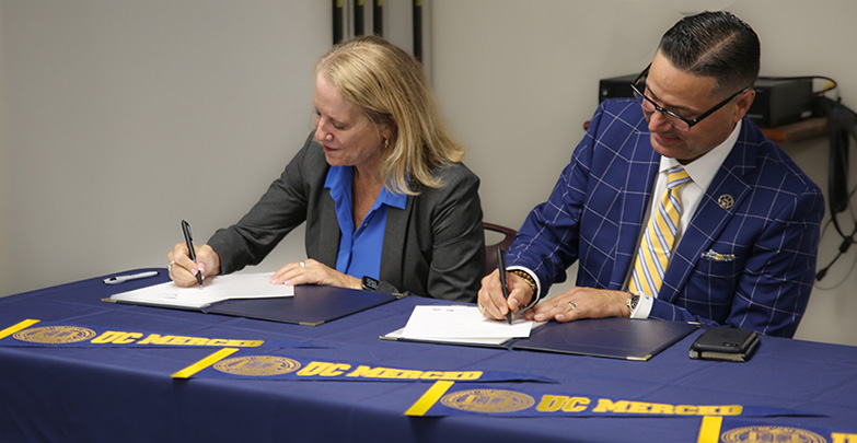 Modesto City Schools Superintendent Sara Noguchi and UC Merced Chancellor Juan Sánchez Muñoz are seen signing documents at a table.