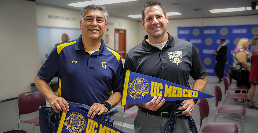 Two people hold up UC Merced pennants.
