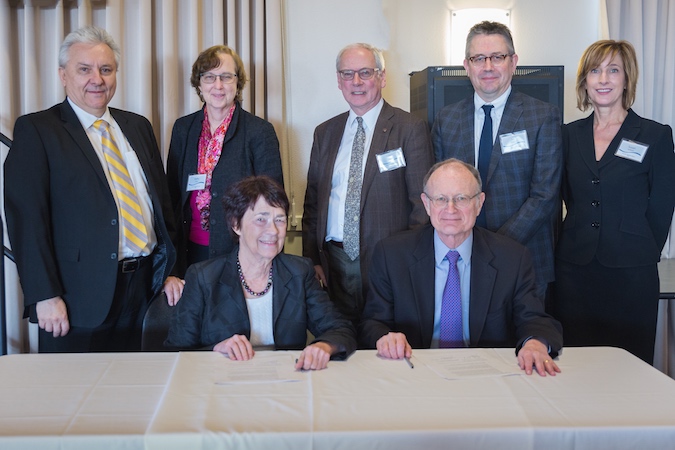 Chancellor Leland and Director Witherell seated at the signing table with five members of the Berkeley Lab delegation standing behind them.