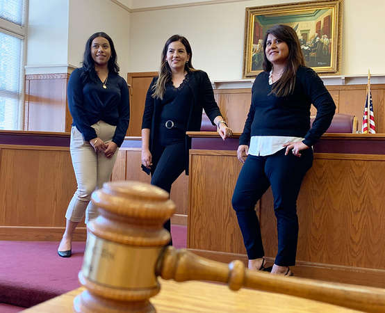 Three women stand next to each other in a mock courtroom.