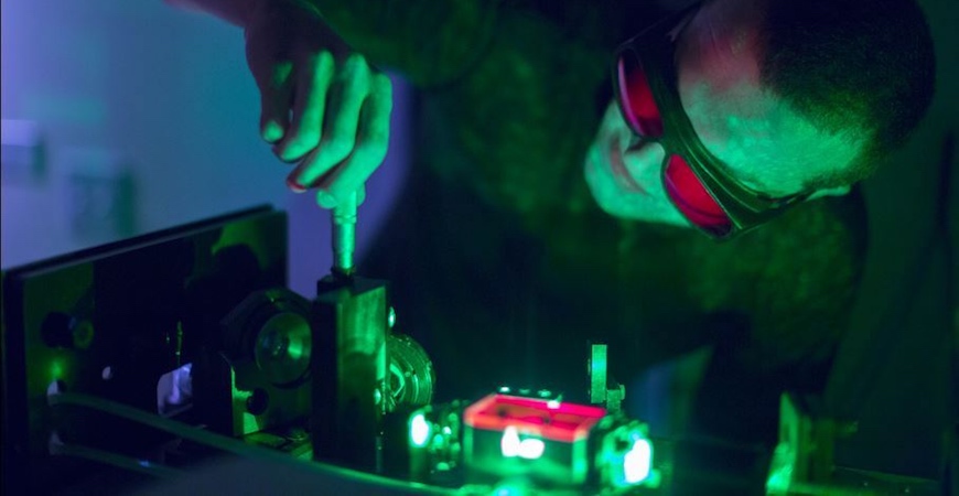 A man wearing safety goggles adjusts a laser apparatus with a screwdriver.