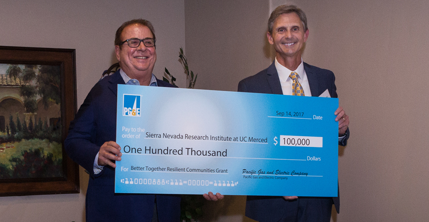 Two men pose with an oversized check on stage at a check presentation ceremony for the PG&E award to SNRI.