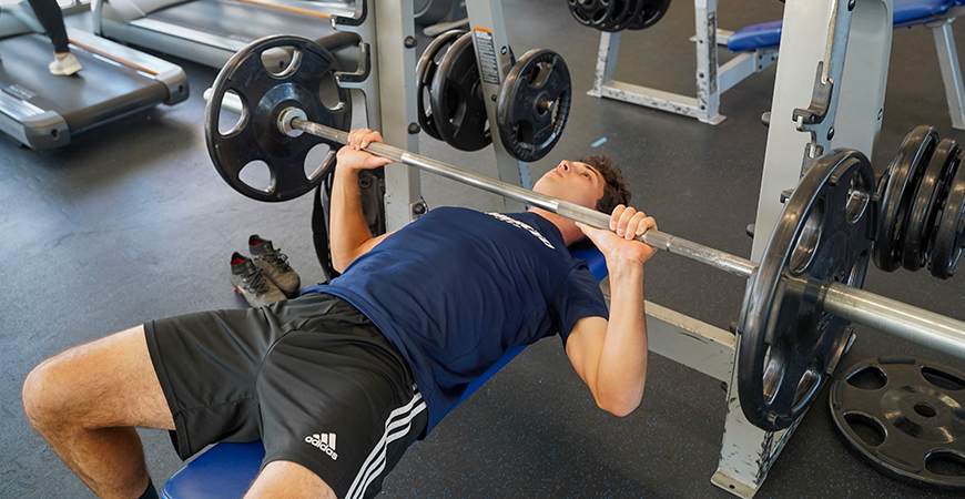 UC Merced student Edwin Casillas bench presses inside a gym.