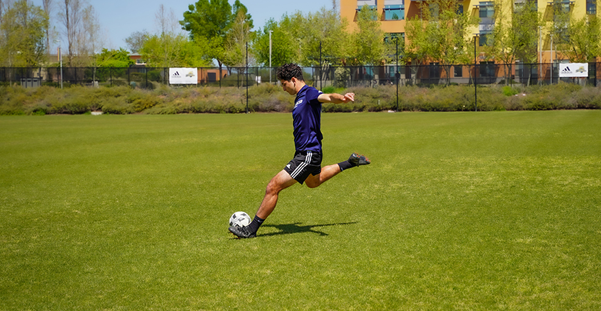 UC Merced student Edwin Casillas kicks a soccer ball on a field.