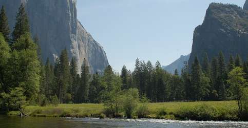 A scenic photo of water, a meadow and rock formations at Yosemite National Park. 